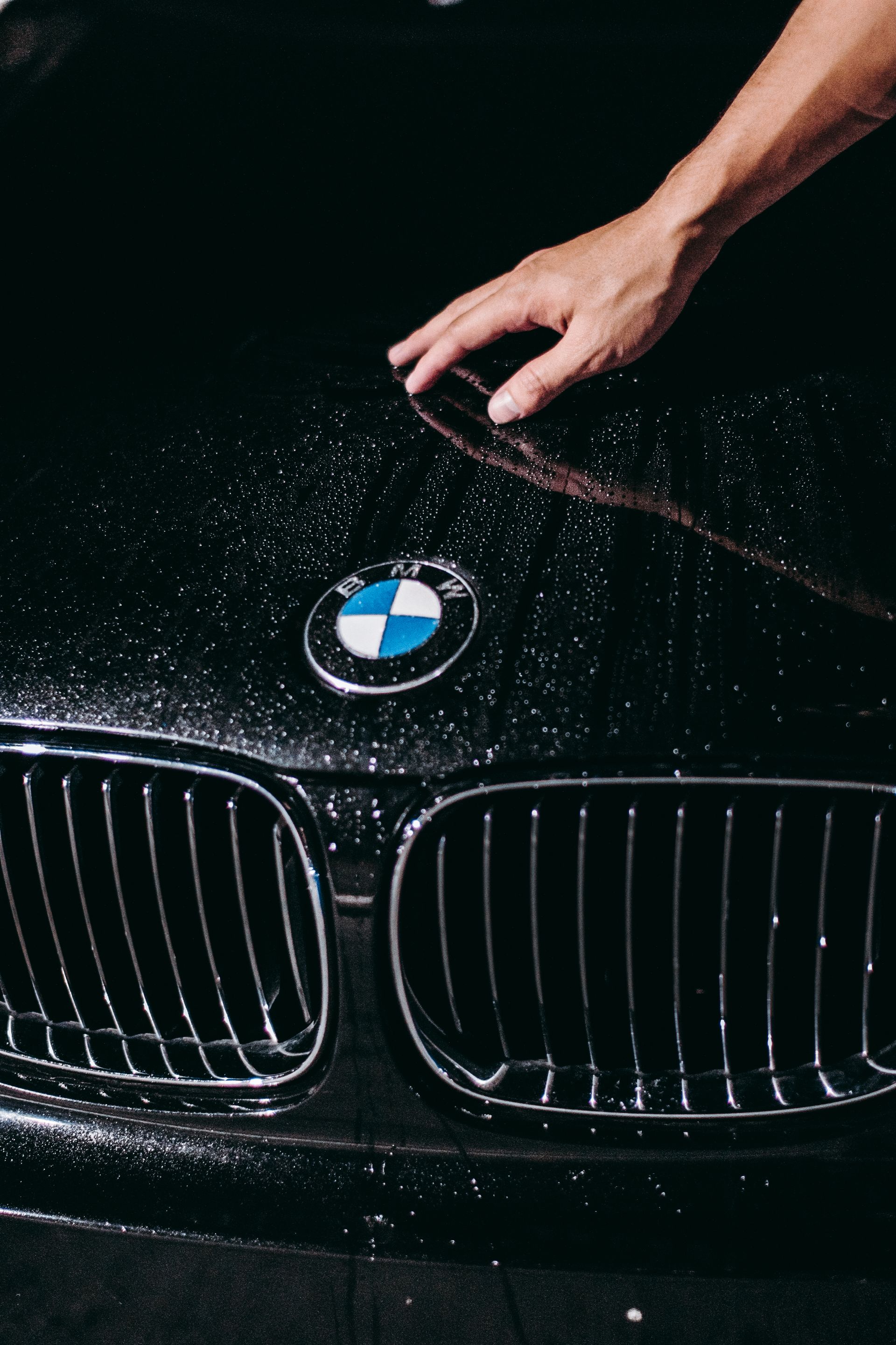 Hand prüft Wassertropfen auf schwarzer Motorhaube